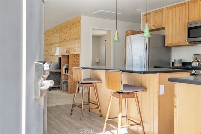 kitchen featuring decorative light fixtures, a breakfast bar area, dark countertops, appliances with stainless steel finishes, and light wood-type flooring