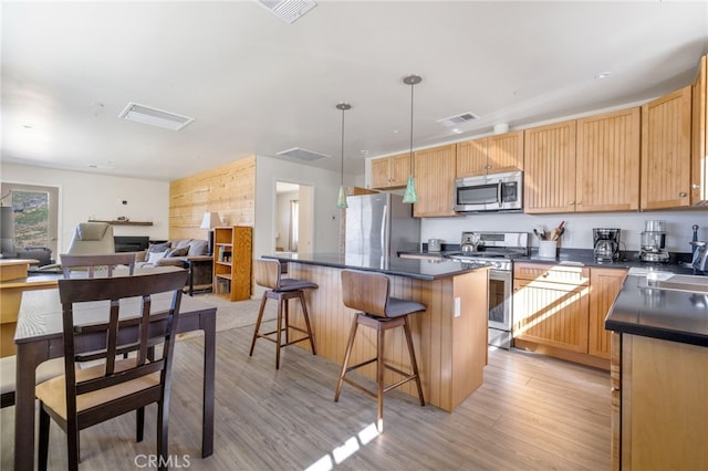kitchen featuring visible vents, dark countertops, light wood-style flooring, appliances with stainless steel finishes, and a breakfast bar area