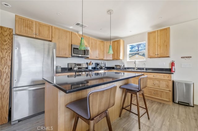 kitchen with light wood finished floors, dark countertops, visible vents, appliances with stainless steel finishes, and a sink