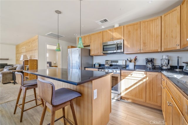kitchen featuring appliances with stainless steel finishes, dark countertops, a kitchen bar, and visible vents