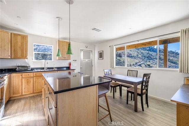 kitchen featuring a sink, visible vents, a kitchen breakfast bar, light wood-type flooring, and dark countertops