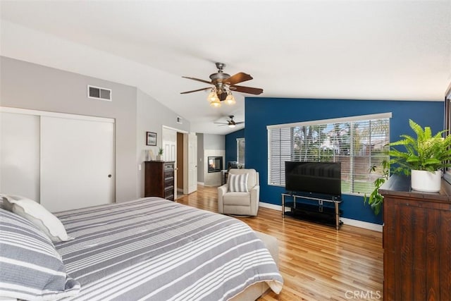 bedroom with light wood finished floors, visible vents, baseboards, vaulted ceiling, and a ceiling fan