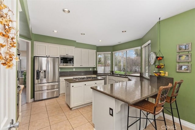 kitchen featuring light tile patterned floors, stainless steel appliances, a peninsula, and white cabinetry