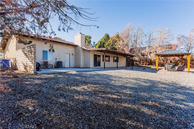 back of property with stucco siding, a chimney, a gazebo, central air condition unit, and a patio area