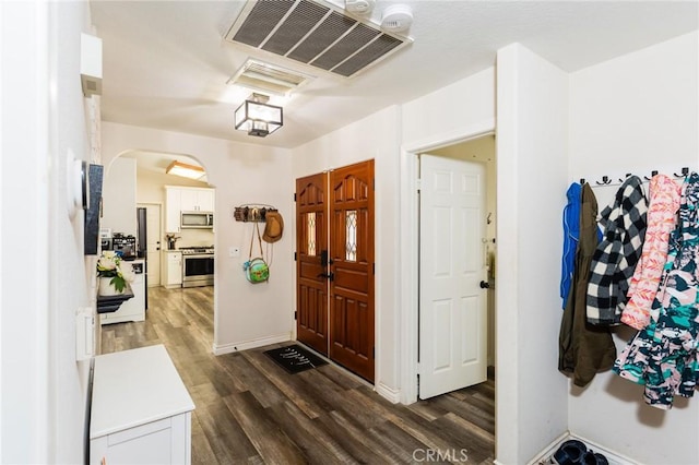 foyer with dark wood finished floors, arched walkways, visible vents, and baseboards