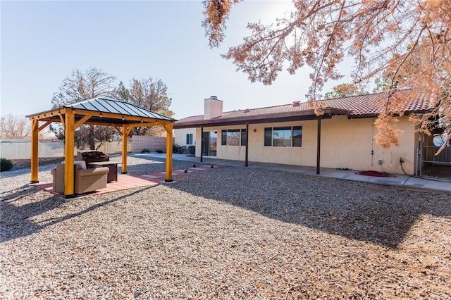 back of house featuring stucco siding, a patio, fence, a gazebo, and a chimney