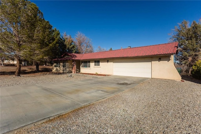 ranch-style home with concrete driveway, a tiled roof, an attached garage, and stucco siding