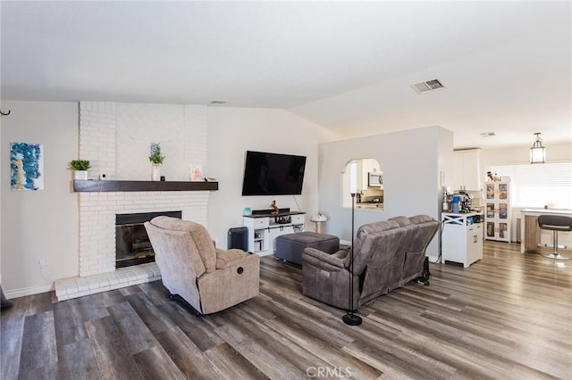 living area featuring visible vents, a brick fireplace, dark wood finished floors, and vaulted ceiling