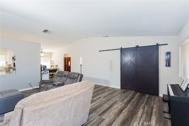 living area with a wealth of natural light, visible vents, dark wood-type flooring, a barn door, and vaulted ceiling