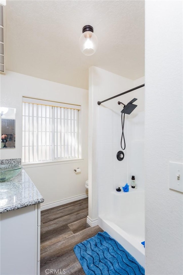 bathroom featuring baseboards, walk in shower, toilet, wood finished floors, and vanity