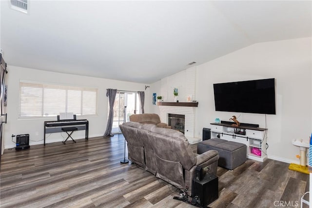 living room featuring lofted ceiling, a brick fireplace, wood finished floors, and visible vents