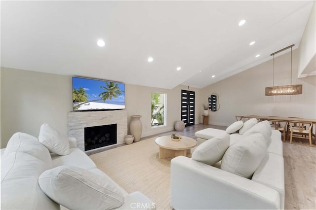 living room with recessed lighting, light wood-type flooring, lofted ceiling, and a stone fireplace