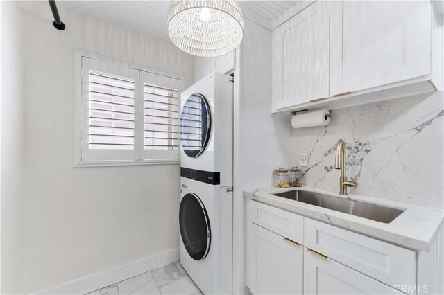 laundry room featuring stacked washer and dryer, marble finish floor, a sink, cabinet space, and baseboards