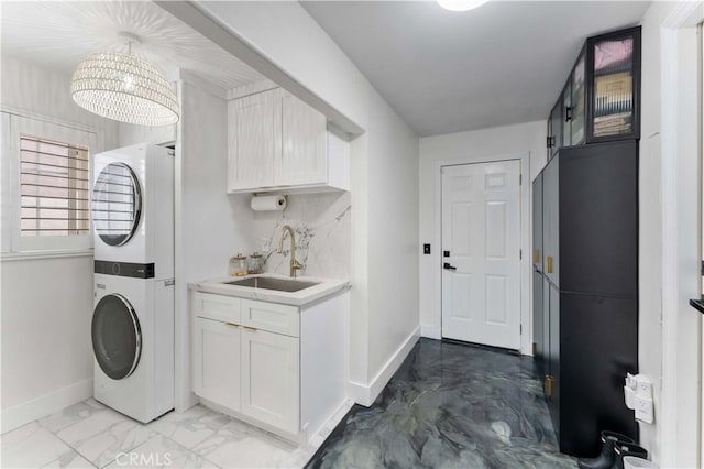 laundry area featuring a sink, baseboards, marble finish floor, and stacked washing maching and dryer