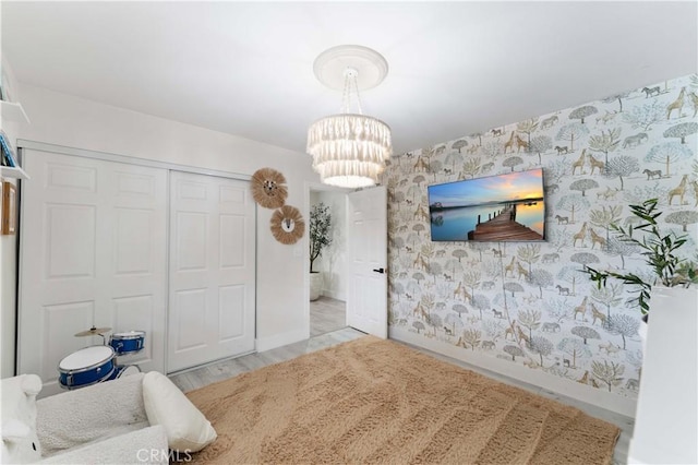 bedroom featuring wood finished floors, baseboards, wallpapered walls, a closet, and a notable chandelier