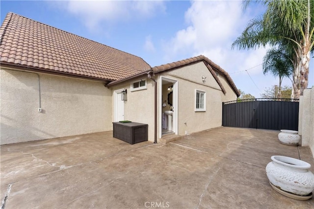 rear view of house with a tiled roof, a gate, a patio area, and stucco siding