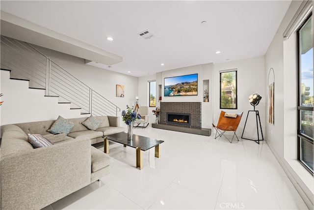 living area featuring tile patterned floors, visible vents, recessed lighting, stairway, and a brick fireplace