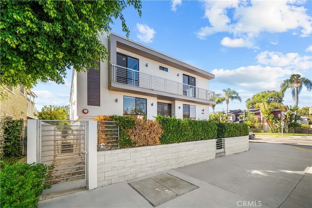 townhome / multi-family property with a balcony, a gate, fence, and stucco siding