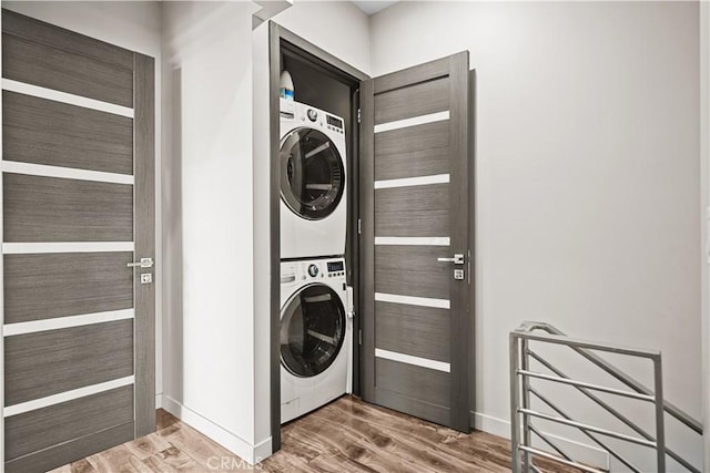 washroom featuring laundry area, stacked washer / dryer, wood finished floors, and baseboards