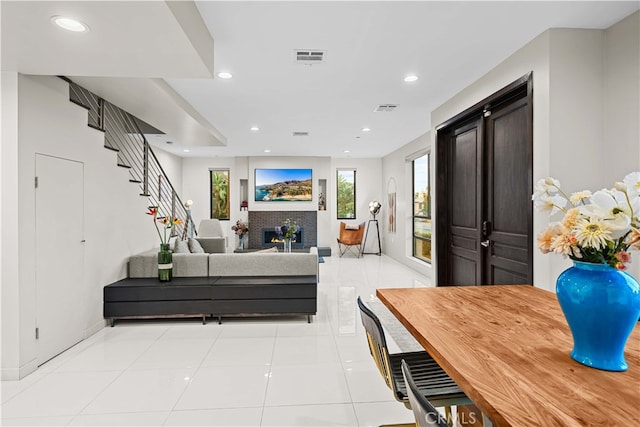 living room featuring visible vents, a warm lit fireplace, recessed lighting, stairway, and light tile patterned flooring