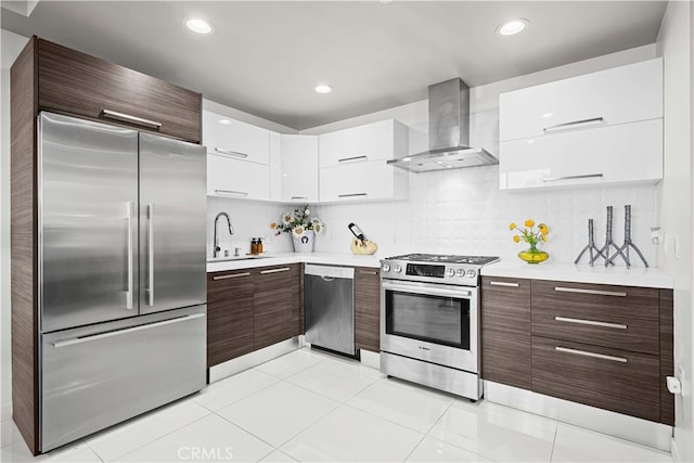 kitchen with a sink, light countertops, appliances with stainless steel finishes, wall chimney exhaust hood, and modern cabinets