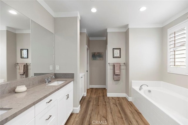 bathroom with ornamental molding, wood finished floors, a garden tub, and a sink