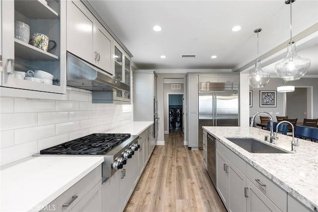 kitchen featuring under cabinet range hood, light wood-type flooring, appliances with stainless steel finishes, washer and dryer, and a sink