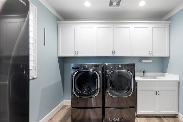 clothes washing area with light wood-style flooring, a sink, cabinet space, separate washer and dryer, and baseboards