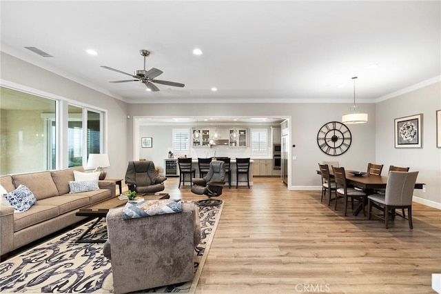 living area featuring baseboards, visible vents, light wood-style flooring, recessed lighting, and crown molding