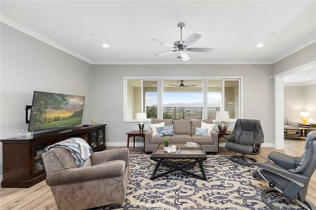 living room with crown molding, a ceiling fan, light wood-type flooring, and baseboards