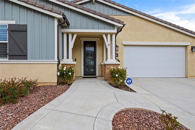 view of exterior entry with stucco siding, a tile roof, board and batten siding, concrete driveway, and an attached garage