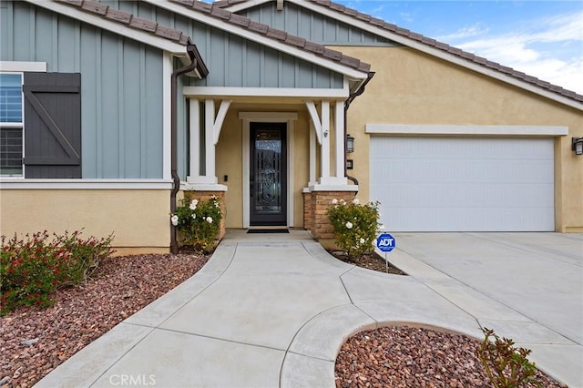 property entrance with stucco siding, driveway, board and batten siding, and an attached garage