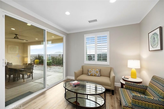 living area with visible vents, baseboards, wood finished floors, and ornamental molding