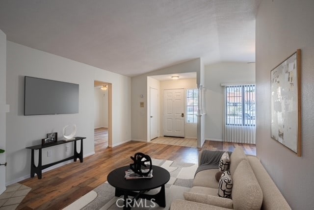 living area featuring lofted ceiling, baseboards, and wood finished floors