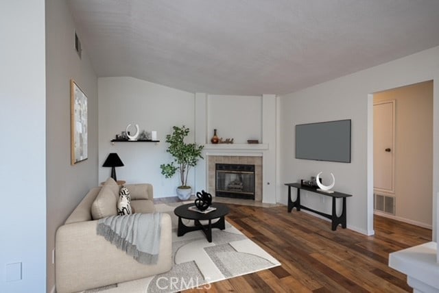 living room featuring a tile fireplace, wood finished floors, visible vents, and baseboards