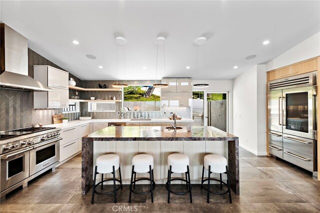 kitchen featuring double oven range, a breakfast bar, wall chimney exhaust hood, and open shelves