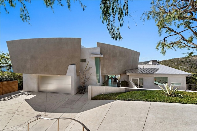 view of front facade featuring concrete driveway, stucco siding, metal roof, a garage, and a standing seam roof