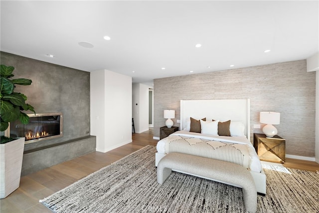 bedroom with an accent wall, a glass covered fireplace, recessed lighting, and wood finished floors