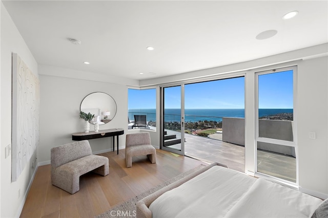 bedroom with wood finished floors, baseboards, recessed lighting, a water view, and access to outside