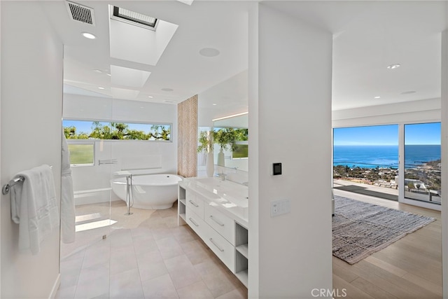 bathroom featuring visible vents, a water view, a freestanding bath, a skylight, and vanity