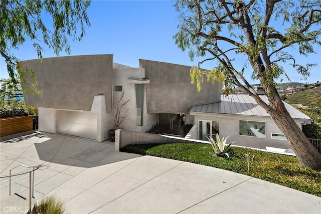 view of front of property with stucco siding, driveway, metal roof, and a standing seam roof