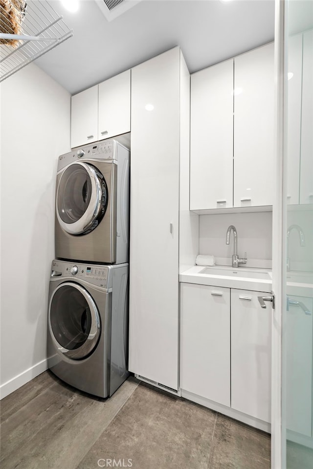 laundry room featuring a sink, cabinet space, baseboards, and stacked washer and dryer