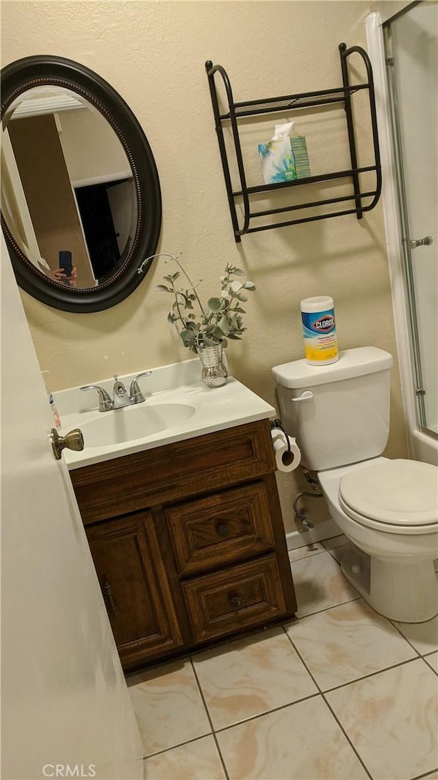 bathroom featuring a shower with door, toilet, vanity, and tile patterned floors