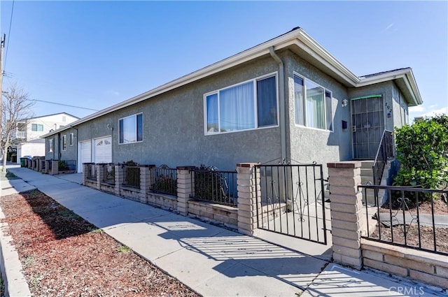 view of side of property with a fenced front yard, stucco siding, and a garage