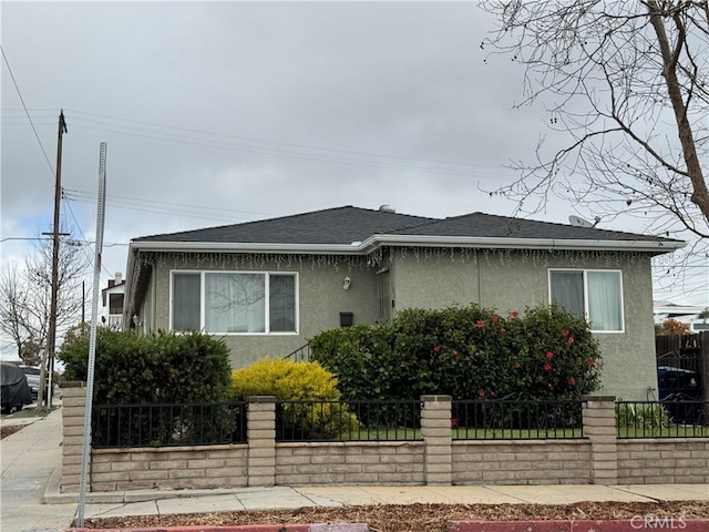 view of front of house featuring a shingled roof, a fenced front yard, and stucco siding