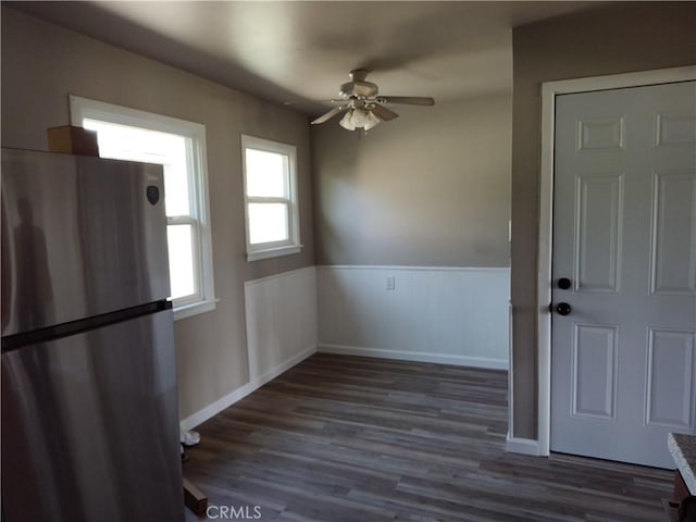 unfurnished dining area with a wainscoted wall, ceiling fan, baseboards, and wood finished floors