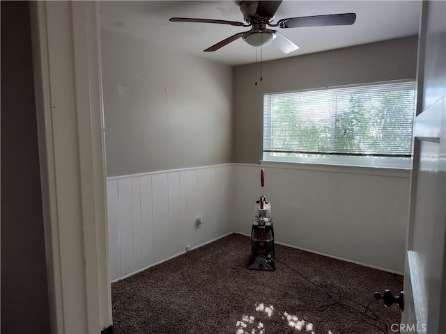 carpeted spare room featuring wainscoting and a ceiling fan