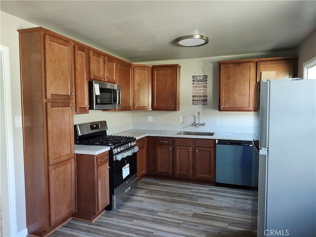 kitchen with brown cabinets, stainless steel appliances, light countertops, a sink, and wood finished floors