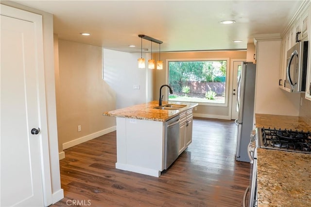 kitchen featuring a center island with sink, a sink, light stone counters, dark wood finished floors, and appliances with stainless steel finishes