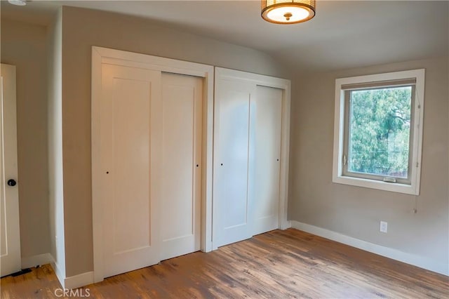 unfurnished bedroom featuring two closets, baseboards, and wood finished floors